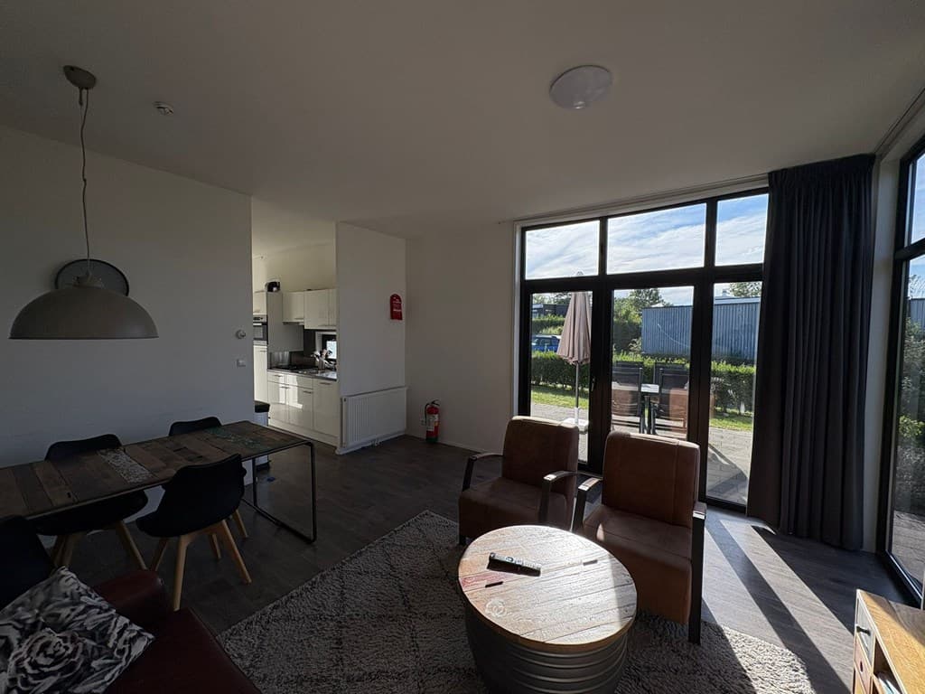 Modern interieur met zithoek, eettafel en keuken in open opstelling, grote ramen bieden veel licht en uitzicht op buitengebie