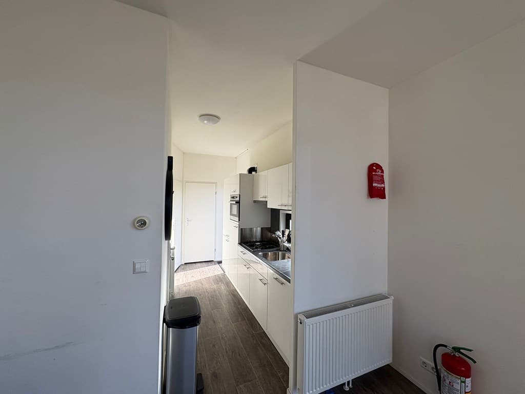 Moderne keuken met wandmeubels, kookplaat en oven, zicht op gang en deur naar andere ruimtes.