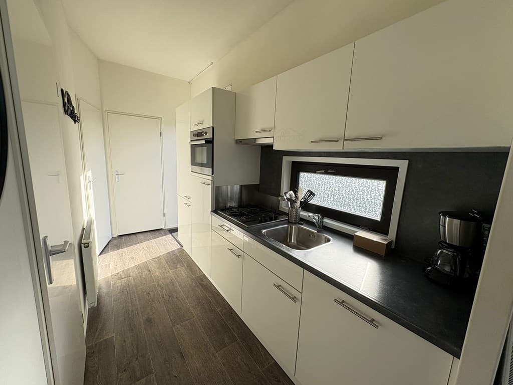 Moderne keuken met ingerichte kasten, een aanrecht met spoelbak en apparatuur zoals een oven en koffiezetapparaat.