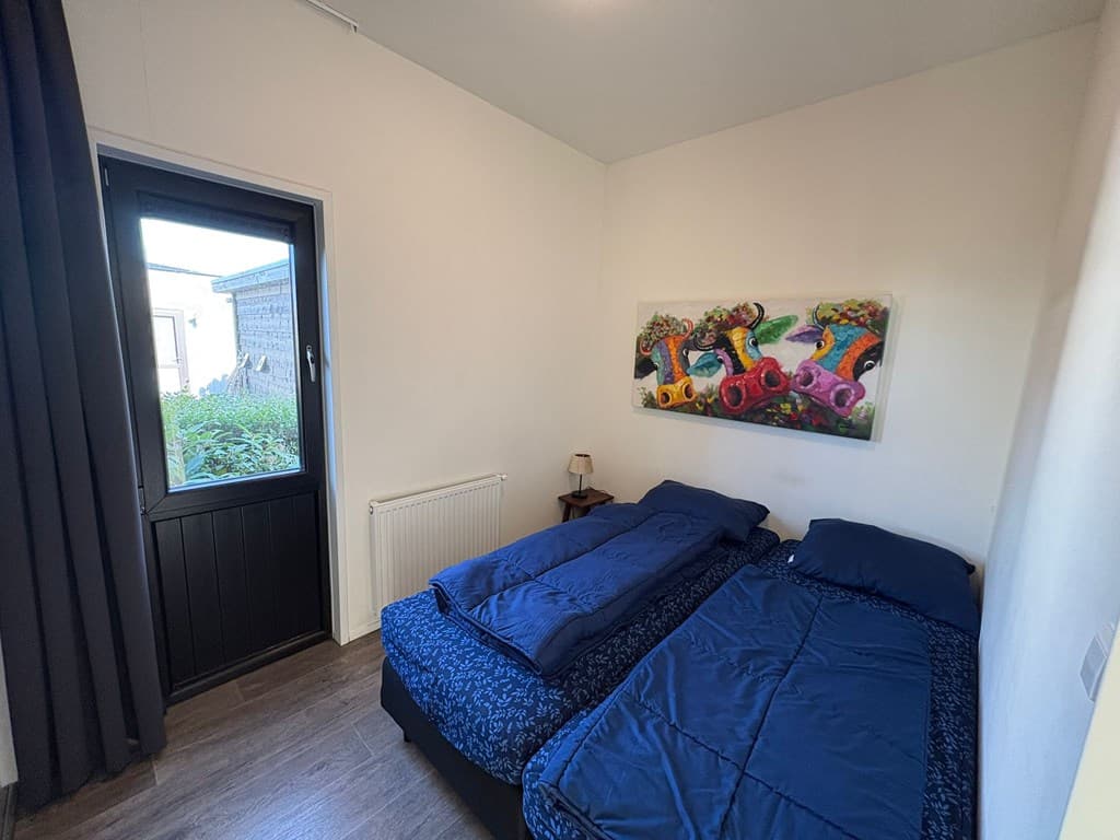 Slaapkamer met twee eenpersoonsbedden, raam met uitzicht op buiten en kleurrijk schilderij aan de muur