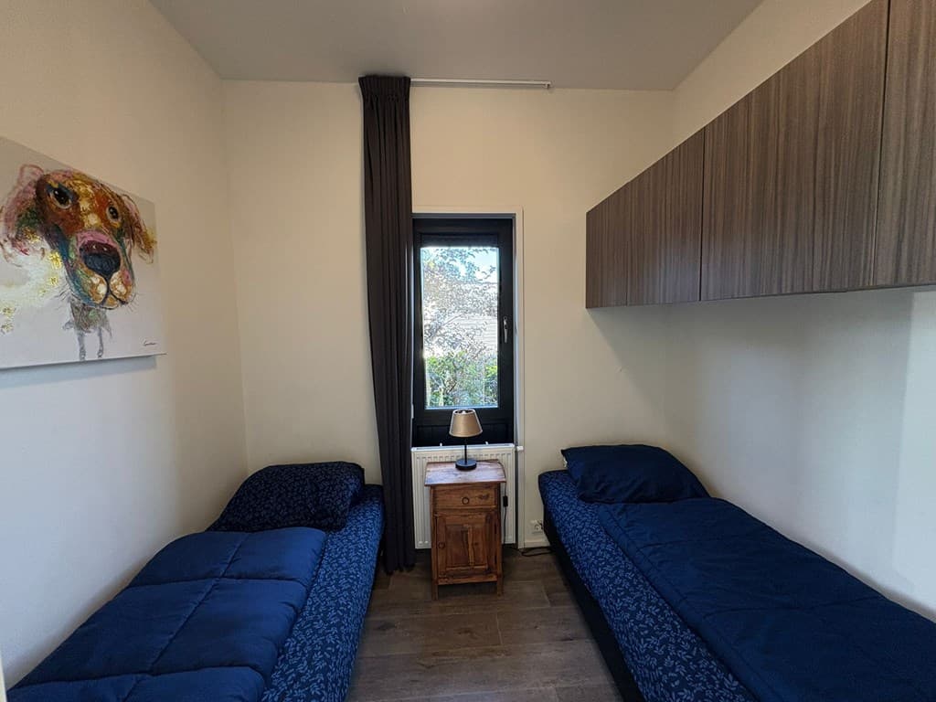 Slaapkamer met twee eenpersoonsbedden, nachttafel en kunst aan de muur naast het raam.