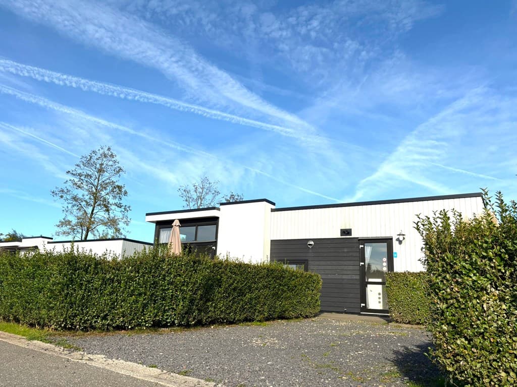 Vakantiehuis met zwarte en witte gevels, omringd door groene heggen en een blauwe lucht met wisbelden.