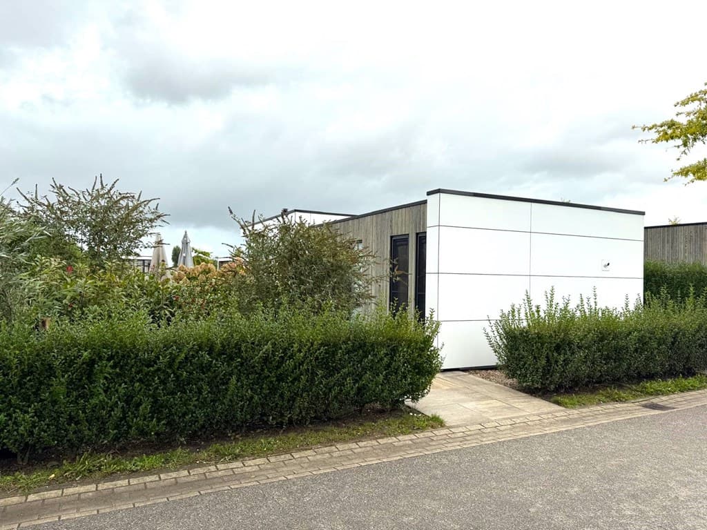 Moderne woning met witte gevel en houten accenten, omgeven door groen en een grindpad.