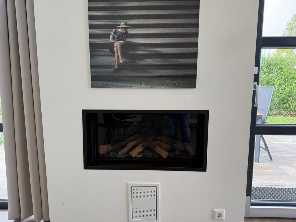Woonruimte met een moderne gashaard en een foto boven de haard, grote ramen met uitzicht op de tuin