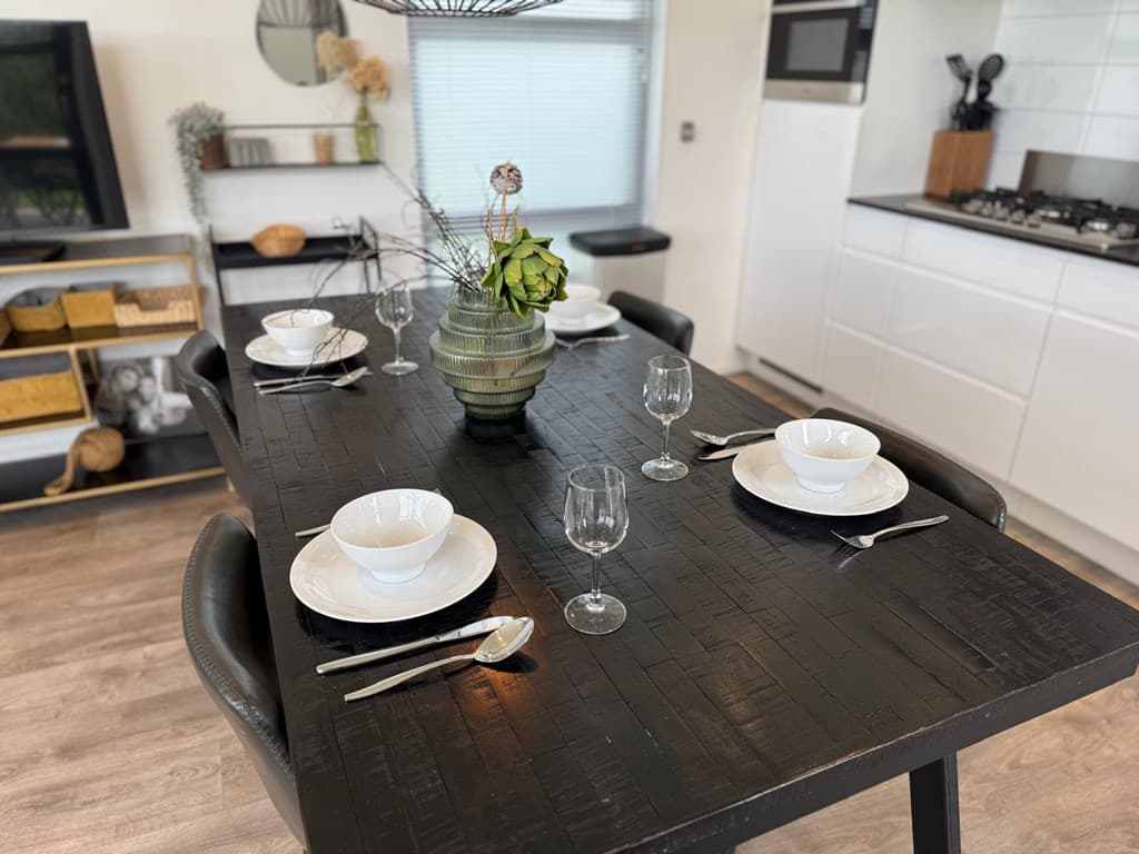 Eettafel met vier borden, bestek en glazen in een moderne woonkamer met keukenopstelling en decoratieve elementen