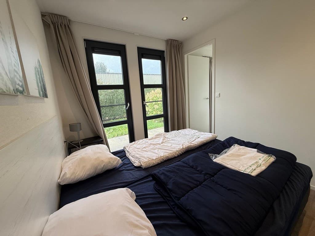 Slaapkamer met twee eenpersoonsbedden, raampartij met uitzicht en natuurlijke lichtinval, gordijnen en een deur naar buiten.
