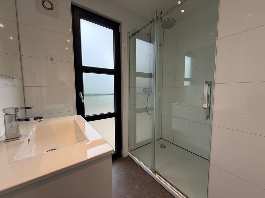 Moderne badkamer met inloopdouche, wastafel en grote raam voor natuurlijk licht.
