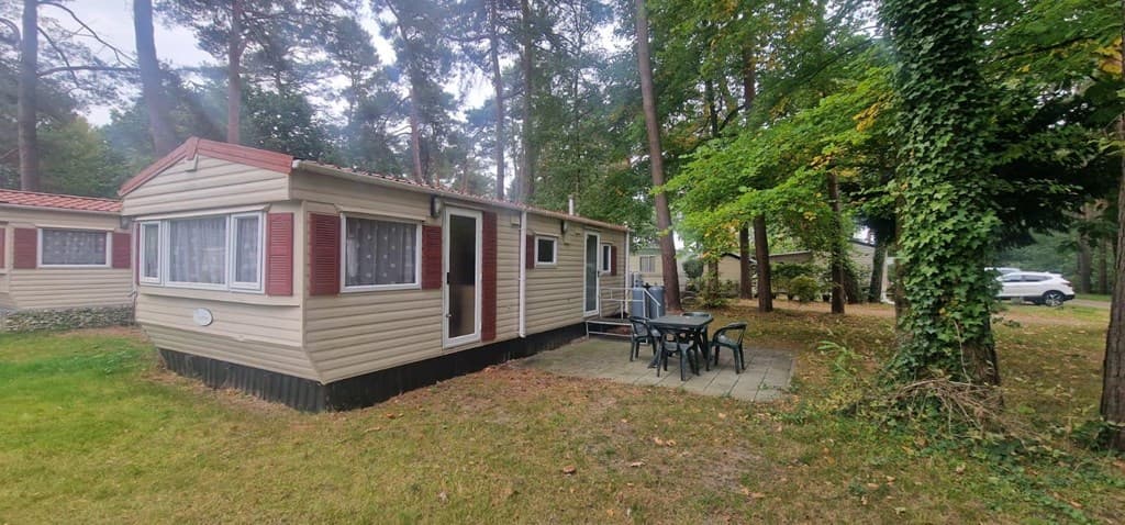Vakantiehuisje in een bosrijke omgeving met een terras en tuinmeubilair, omringd door bomen en andere woningen.