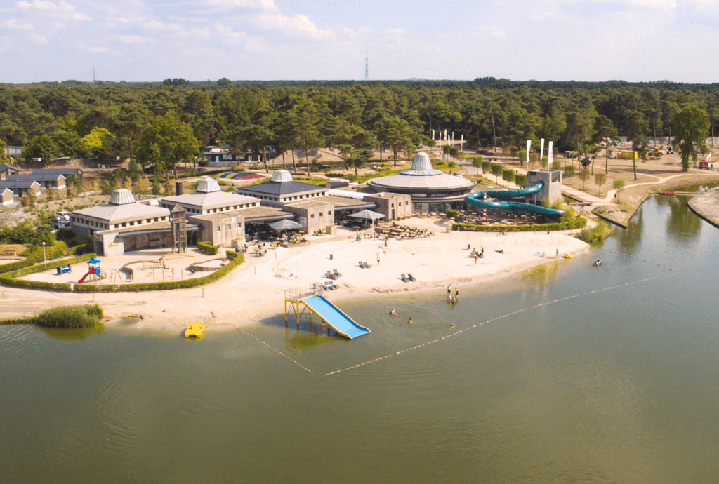 Luchtbeeld van een recreatiegebied met een strand en water, omringd door bomen en gebouwd met moderne faciliteiten.
