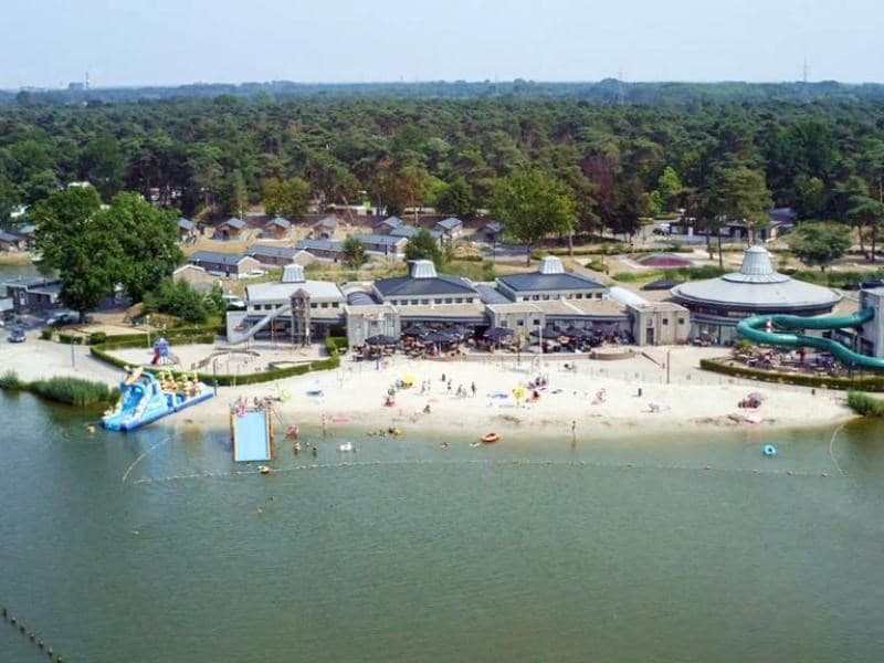 Uitzicht op het strandgebied en water van EuroParcs Zilverstrand met ligstoelen en zwembadglijbaan in de achtergrond