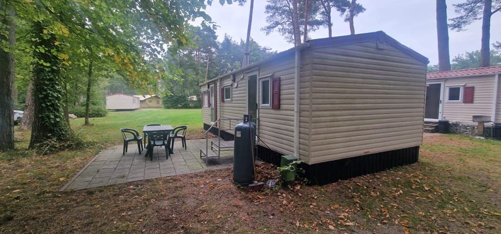Houtachtig buitenaanzicht van een accommodatie met een patio en tuinmeubilair in een bosachtige omgeving.