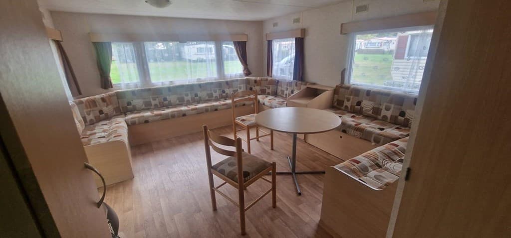 Binnenzijde van een vakantiewoning met een zithoek, tafel en vloerbedekking in een lichte kleur.