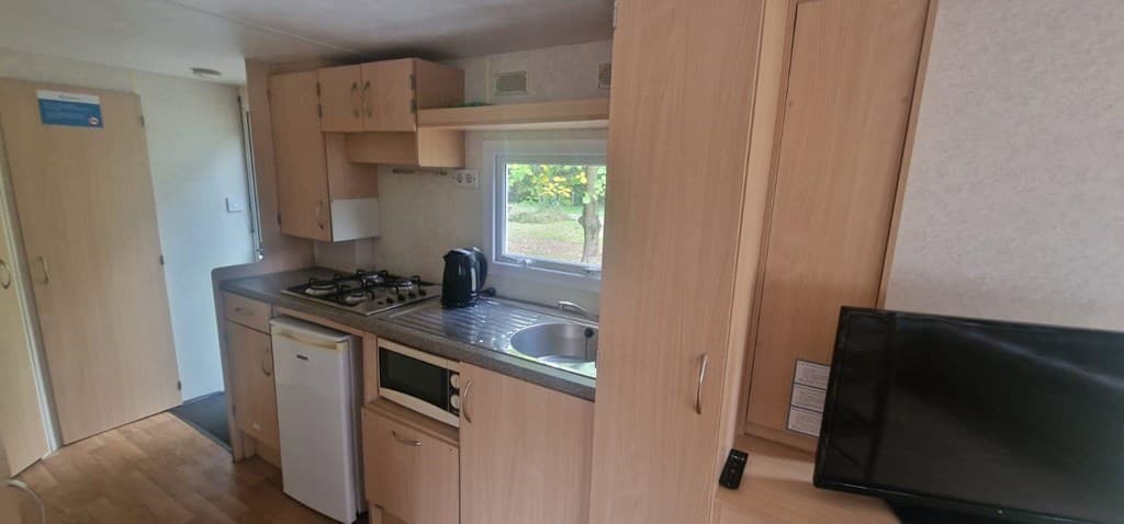 Keuken met houten kasten, gasfornuis, koelkast, spoelbak en tv, met zicht op een groene buitenomgeving