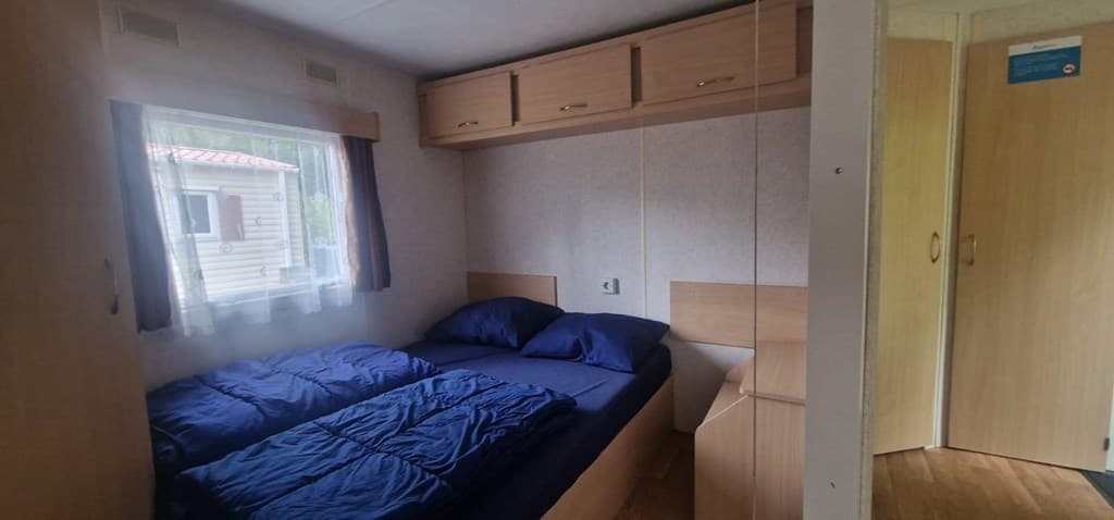 Slaapkamer met twee eenpersoonsbedden, kast en deur naar de gang met lichtinval van het raam.
