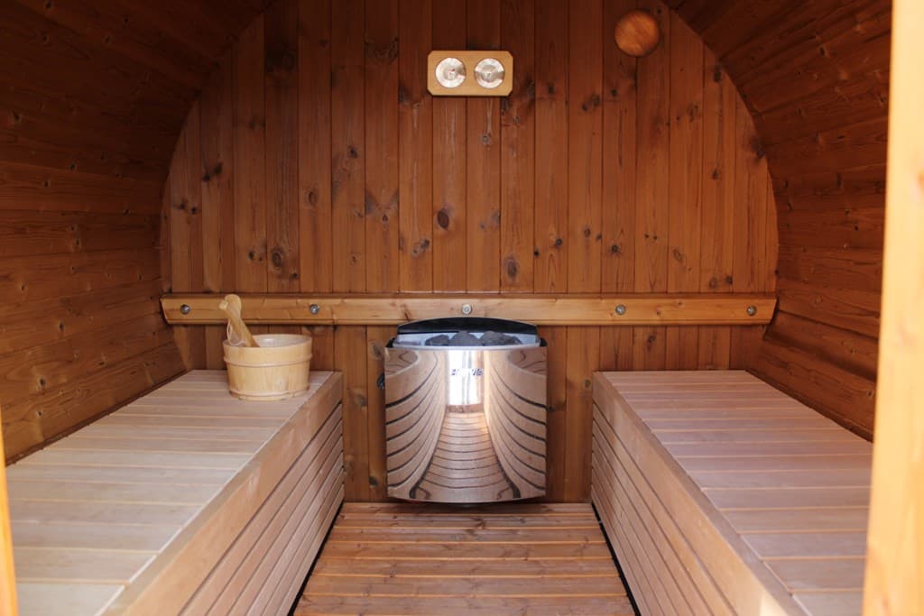 Binnenkant van een sauna met houten wanden, banken en een metalen kachel in het midden.