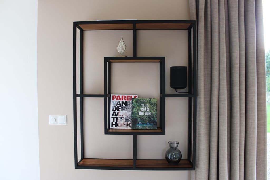 Moderne wandkast met boeken, decoratieve objecten en een vaas, tegen een lichte muur met gordijnen.