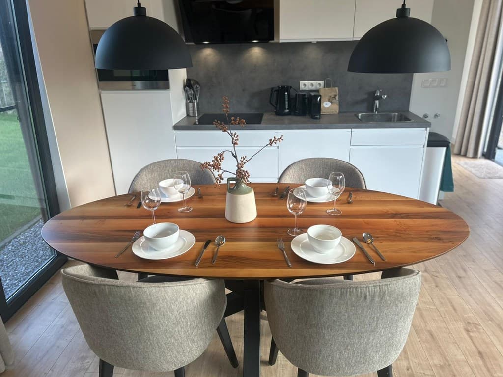 Eetkamer met een ovaal houten tafel, vier stoelen, en een moderne keuken op de achtergrond met witte kasten en apparatuur