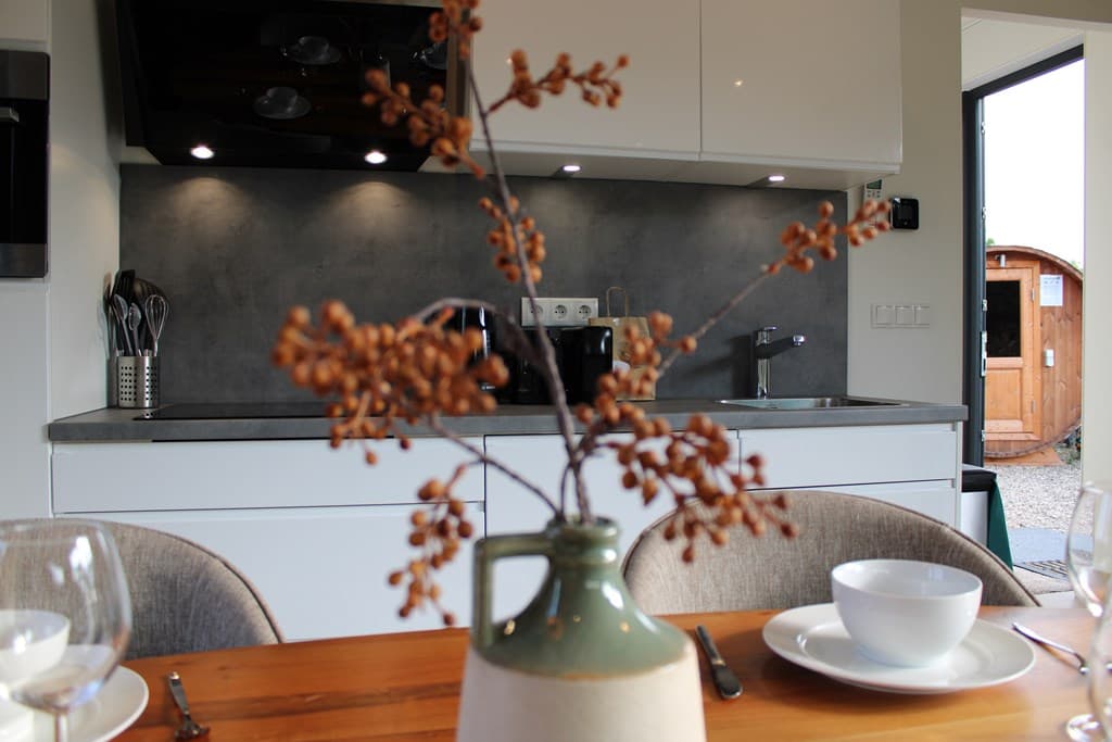 Moderne keuken met grijze wand, ingebouwde apparatuur en eettafel met servies en een vaas met takken op de voorgrond