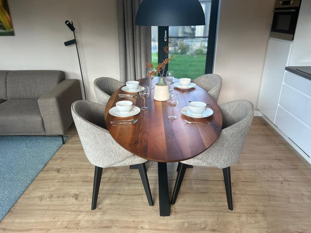 Eettafel met vier stoelen, servies en glazen, gesitueerd in een moderne en lichte woonkamer met een uitzicht op groen.