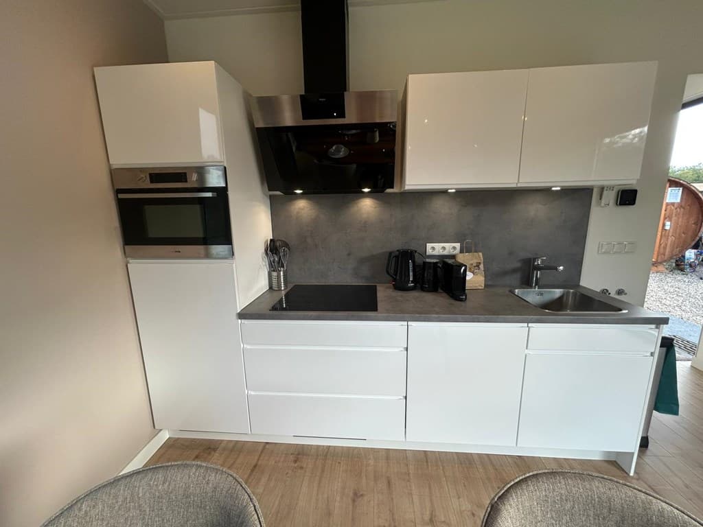 Moderne keuken met witte kasten, inbouwoven, afzuigkap en aanrecht met spoelbak en koffiezetapparaat.