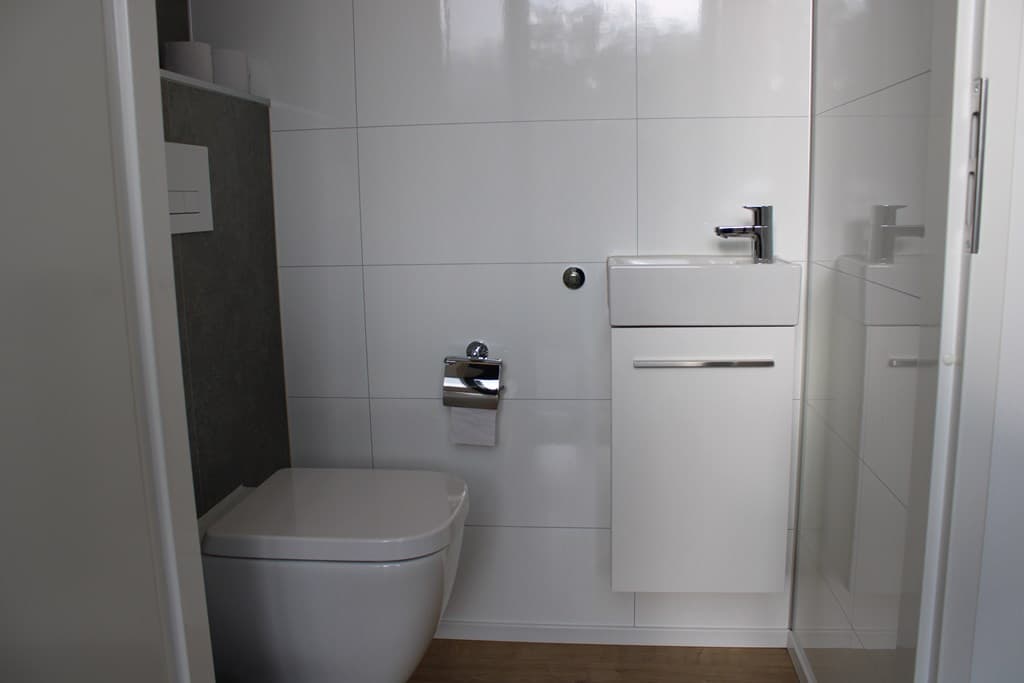 Moderne badkamer met toilet, wastafel en inloopdouche in neutrale kleuren en lichtinval.