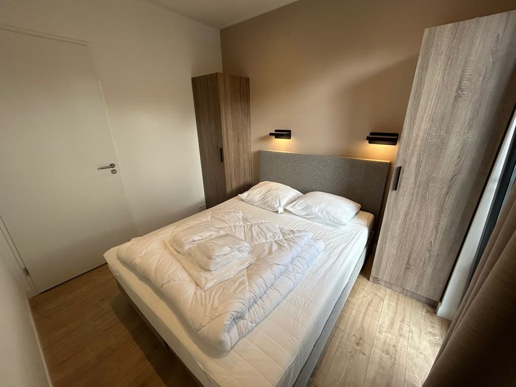 Slaapkamer met een tweepersoonsbed, nachtkastjes en inbouwkasten in een neutrale kleur.