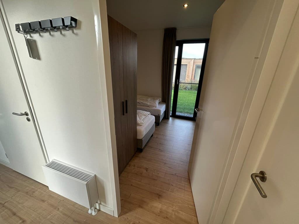 Ingang van een slaapkamer met twee eenpersoonsbedden en zicht op de tuin door een glazen deur.