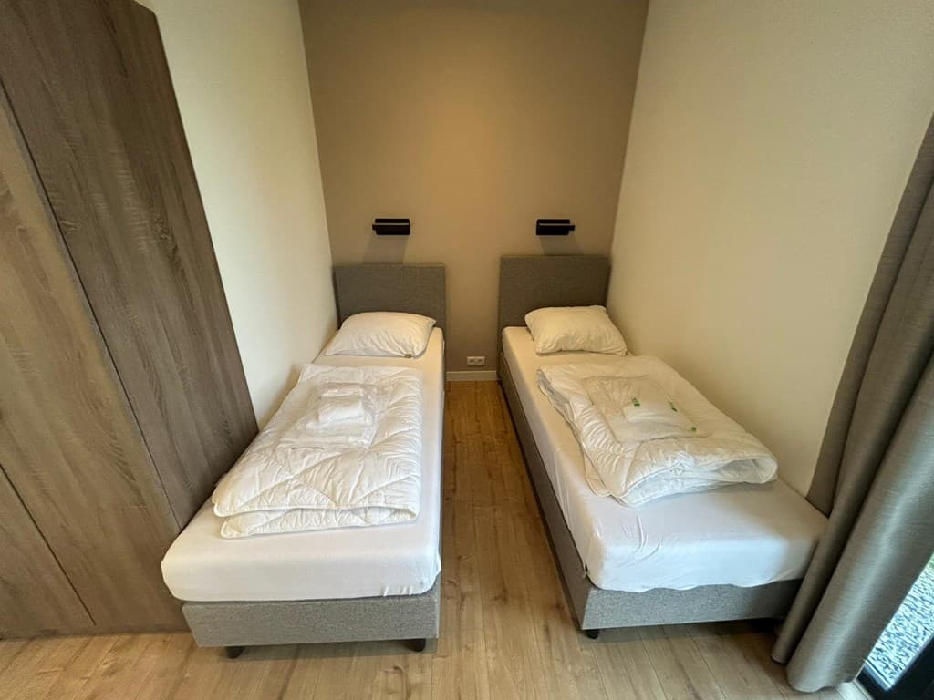 Slaapkamer met twee eenpersoonsbedden, wandlampen en een kast in neutrale kleuren met houten vloer