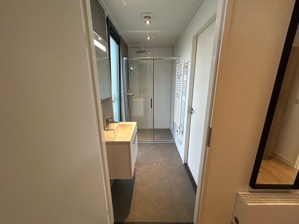 Moderne badkamer met inloopdouche, wastafel en handdoekenradiator, lichte tegelwanden en vloer.