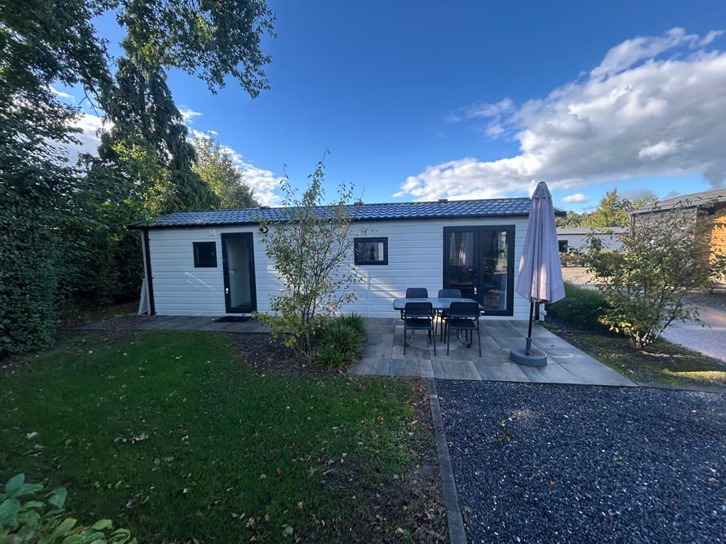Vakantiewoning met een terras, tuin en parasol, gelegen tussen bomen bij EuroParcs Zuiderzee.