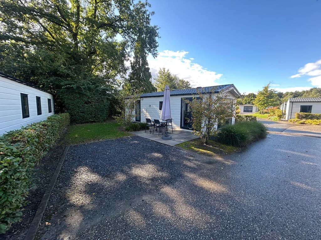 Vakantiehuis met zitje en parasol, omgeven door groen en stenen pad in EuroParcs Zuiderzee.