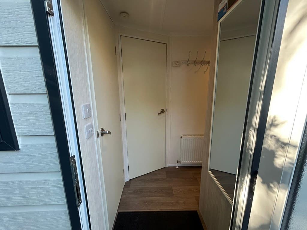 Ingang van een woning met een deur, wandhaken en een spiegel aan de rechterzijde.