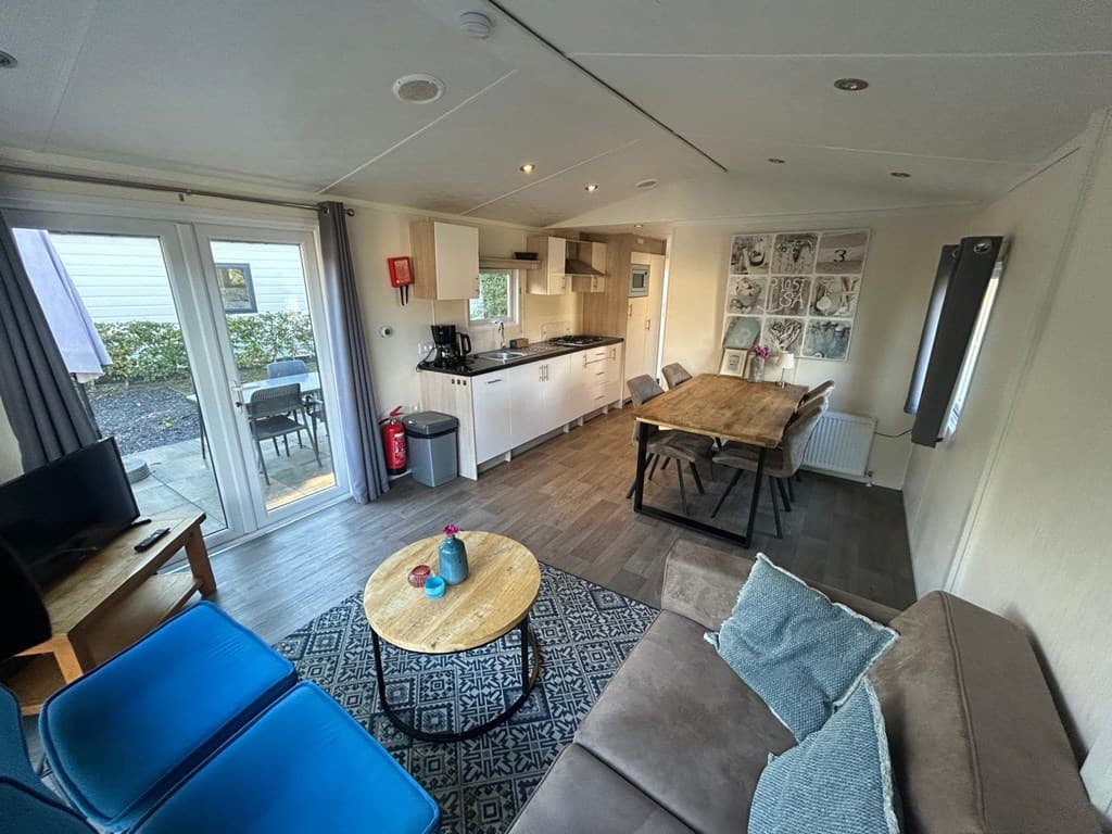 Lichte woonkamer met open keuken, eettafel, zithoek en toegang tot het terras via dubbele deuren.