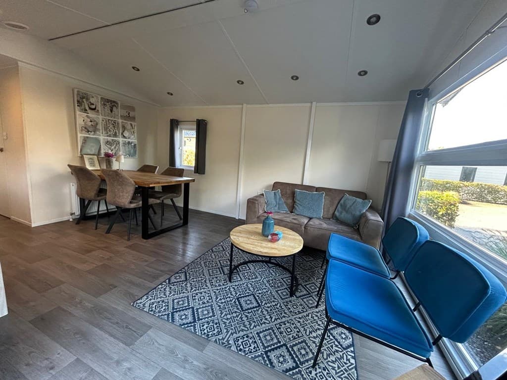 Gezellige woonkamer met een bank, eettafel, blauwe stoelen en een kleurrijk vloerkleed in EuroParcs Zuiderzee.