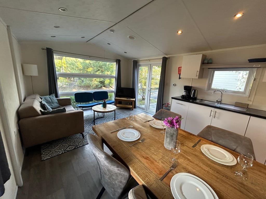 Woonkamer met een eettafel, keuken, zithoek en grote ramen met uitzicht op de tuin