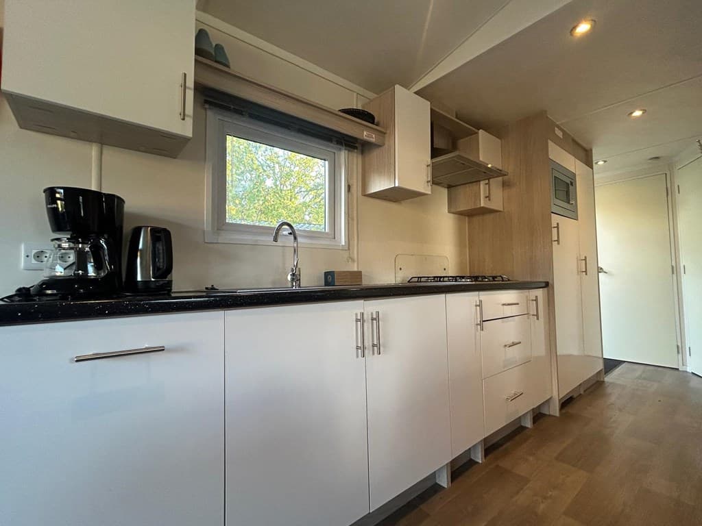 Moderne keuken met witte kasten, zwarte aanrecht en apparatuur zoals een koffiezetapparaat en kookplaat.
