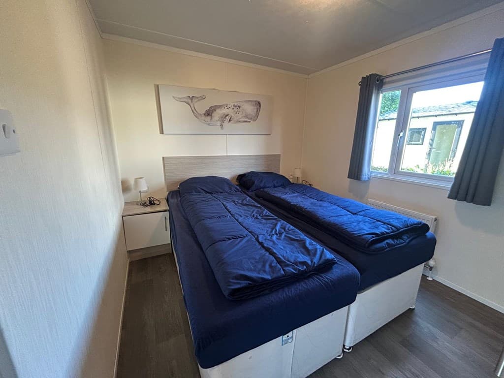 Slaapkamer met twee eenpersoonbedden, uitzicht op buiten door het raam en een walvis schilderij aan de muur