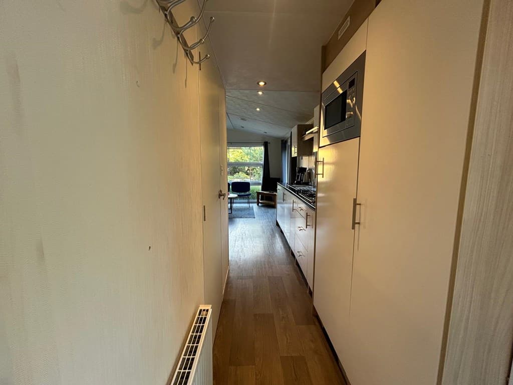 Helle hal met houten vloer, keuken aan de rechterkant en zicht op een gezellige woonkamer aan het einde van de gang