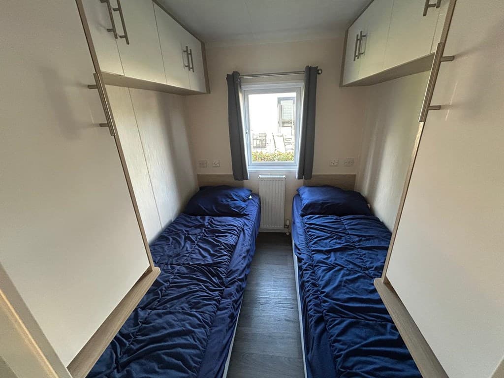 Slaapkamer met twee eenpersoonsbedden en kastjes, zichtbaar raam met uitzicht op buitenruimte.