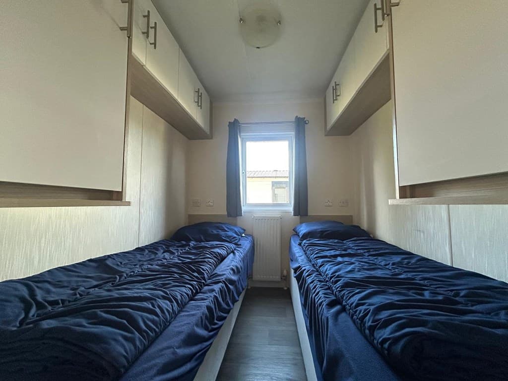 Slaapkamer met twee eenpersoonsbedden, boven verlichting en kasten aan de wand, raam met uitzicht naar buiten.