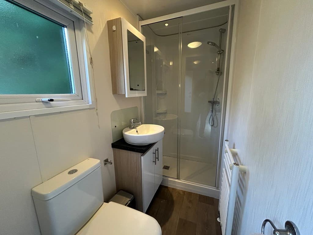 Badkamer met douche, wastafel en toilet, voorzien van een raam en lichte wandafwerking