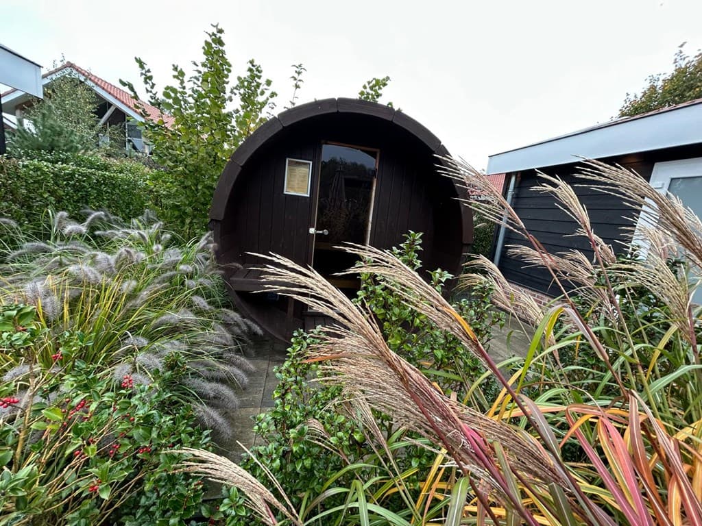 Houten accommodatie in een tuin met weelderige planten en siergras rondom, bij Résidence Lichtenvoorde.
