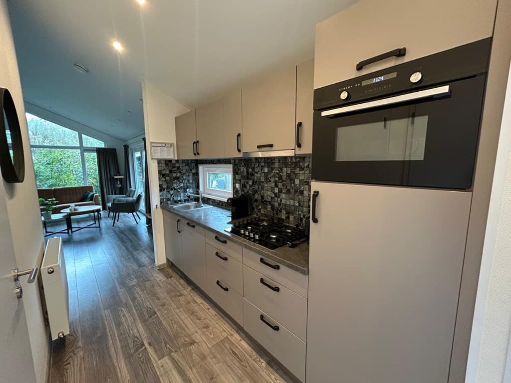 Moderne keuken met inbouwapparatuur, kastjes in neutrale kleuren en tegelachterwand met mozaïekdetails.