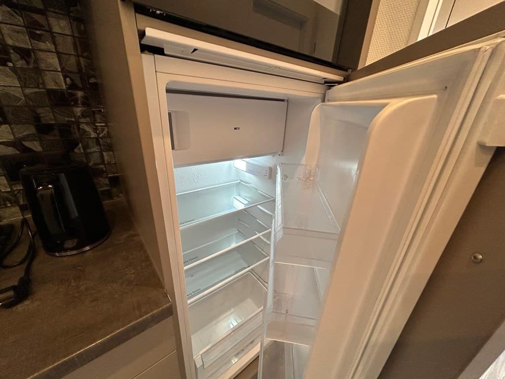 Ingerichte koelkast met een transparant interieur en enkele planken, naast een ketel op het aanrecht.