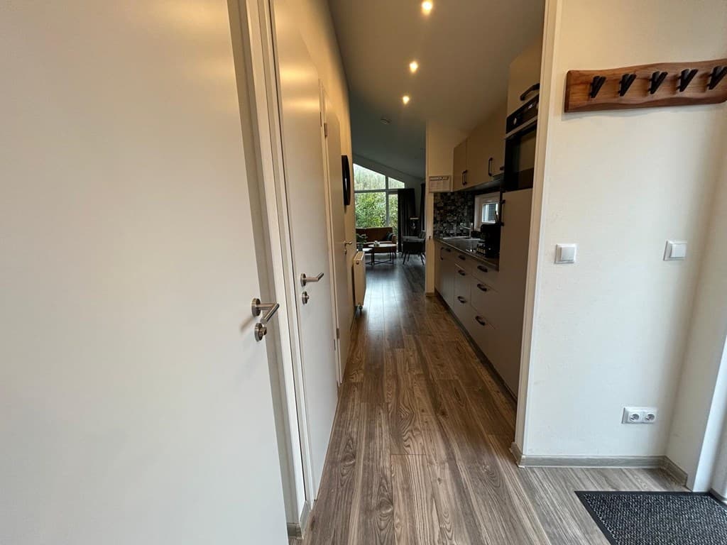 Lichte gang met toegang tot een keuken en een zitgedeelte, met houten vloeren en moderne inrichting