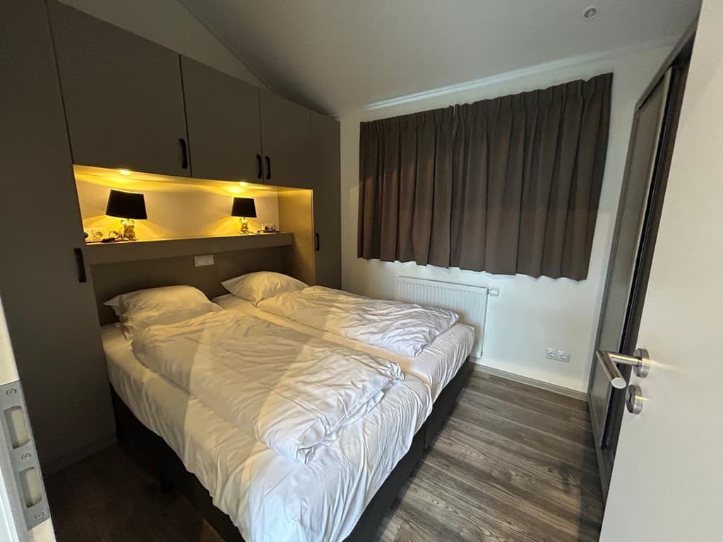 Slaapkamer met twee aparte bedden, nachtelijke verlichting en een groot raam met gordijnen.