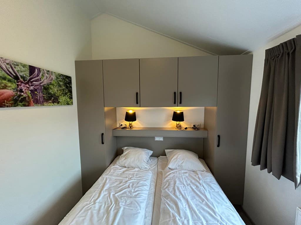 Slaapkamer met twee losse bedden, nachtkastjes met lampen en opbergkasten aan de muur.