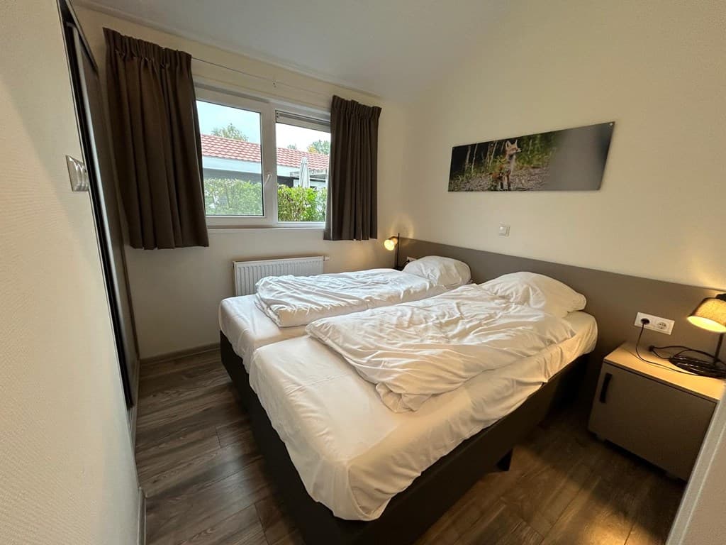 Slaapkamer met twee eenpersoonsbedden, raam met uitzicht op buiten en nachtkastje met lamp.
