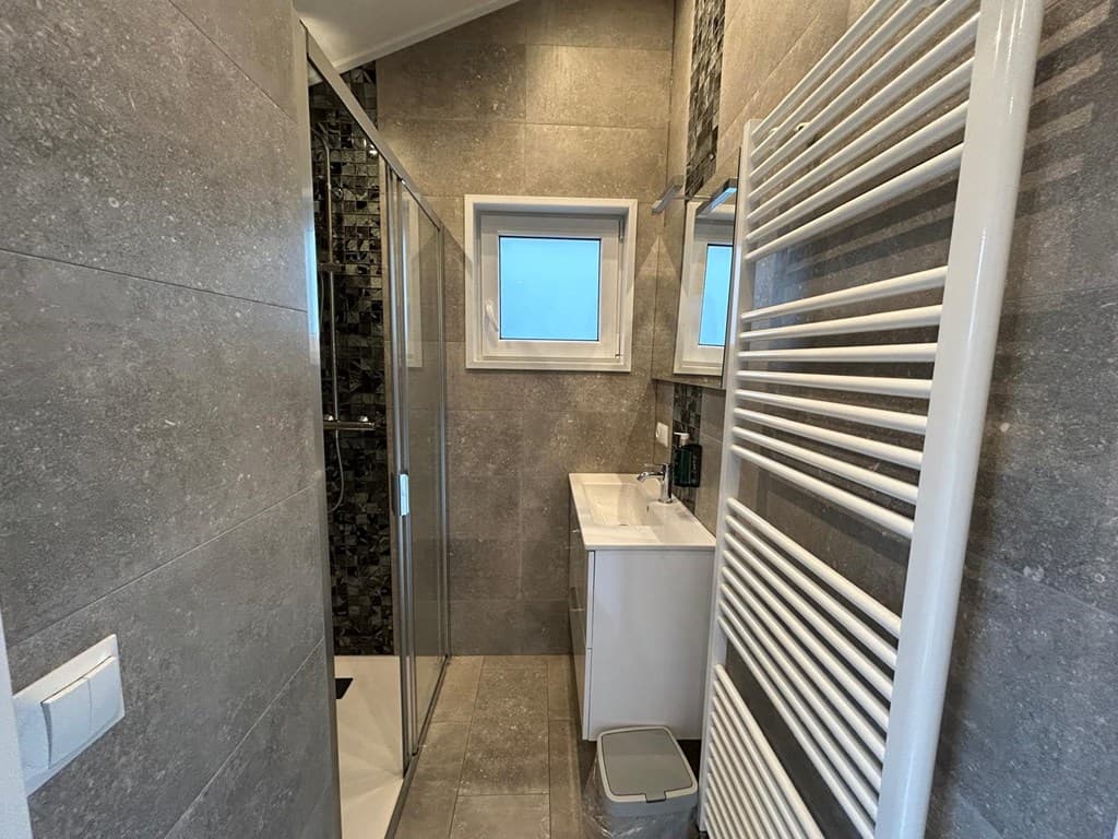 Moderne badkamer met douche, wastafel en handdoekradiator, volledig betegeld in neutrale kleuren