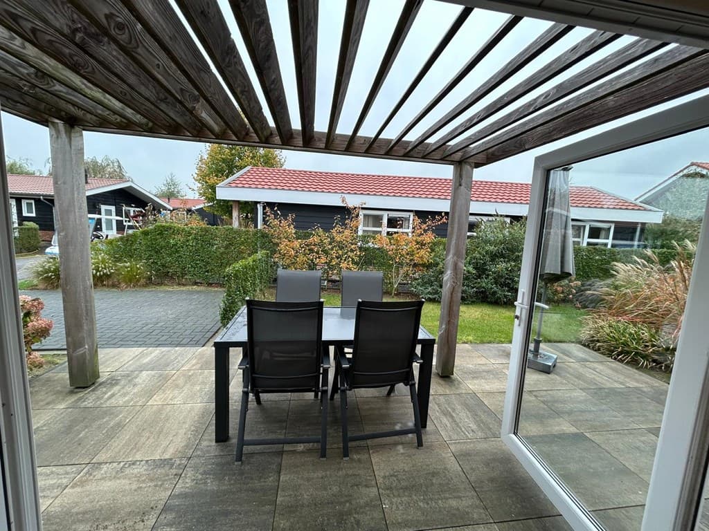 Terras met vier stoelen en een tafel, omgeven door een tuin en zicht op andere woningen in een parkachtige omgeving
